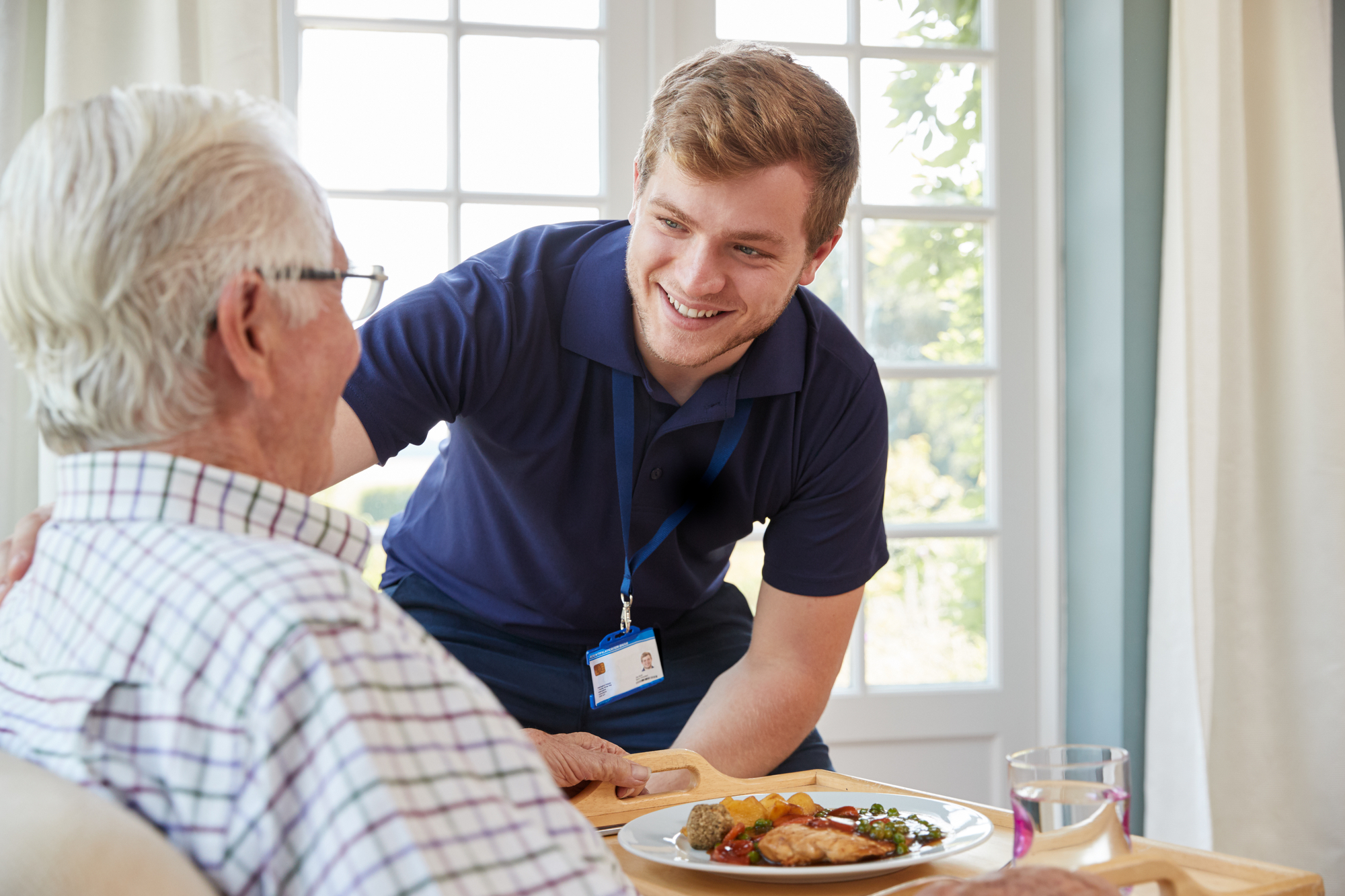 Caregiver assisting elderly man and serving a meal